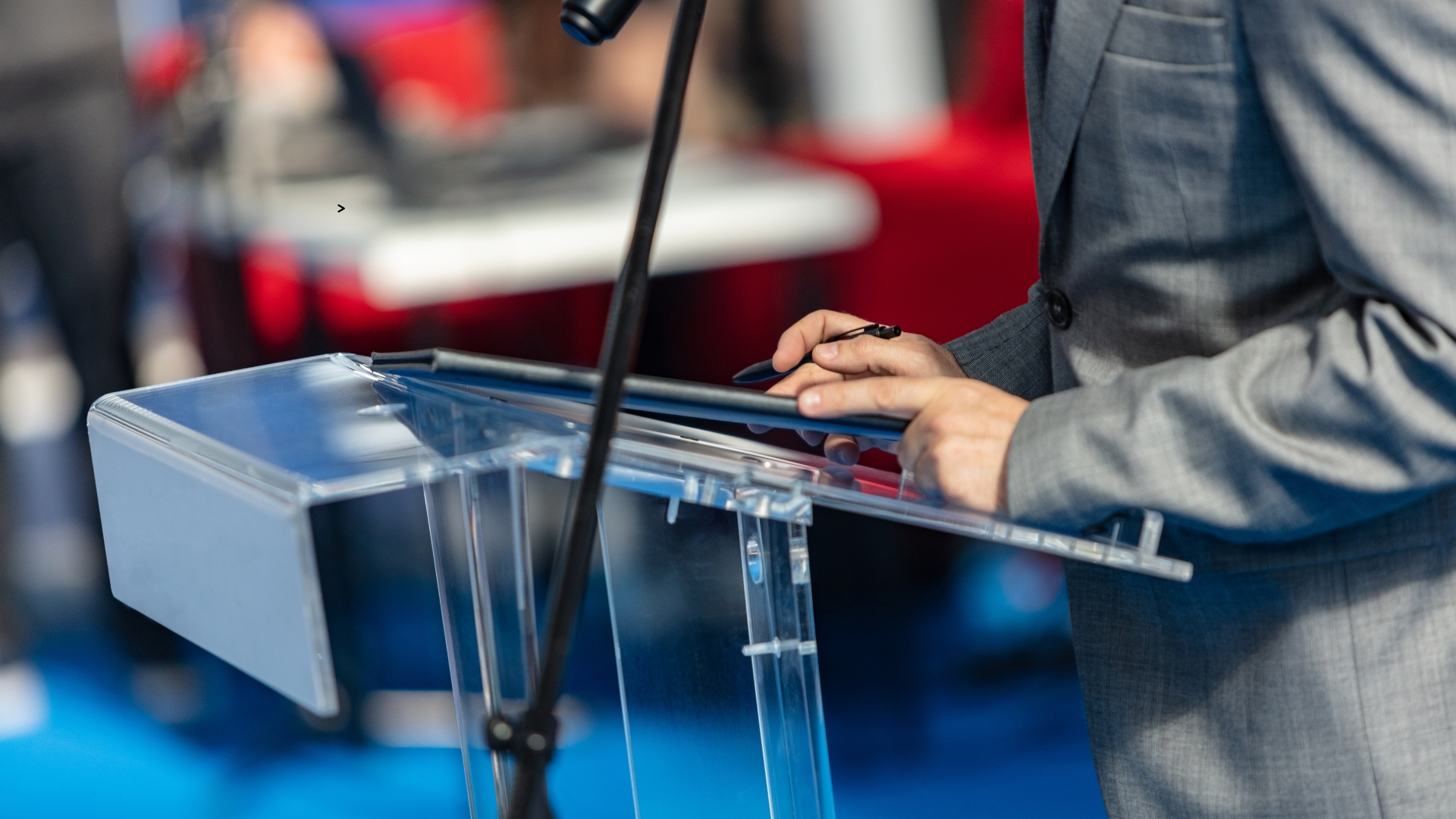 Un plan rapproché sur les mains d'un homme se tenant en face d'un pupitre avec un microphone.